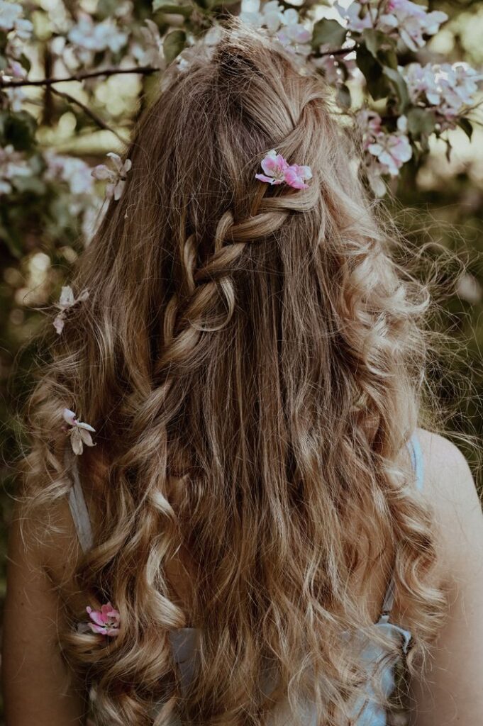pexels photo 11497210 A woman with braided long hair adorned with flowers, viewed from behind.