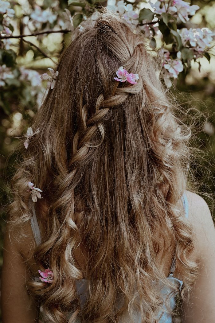 A woman with braided long hair adorned with flowers, viewed from behind.