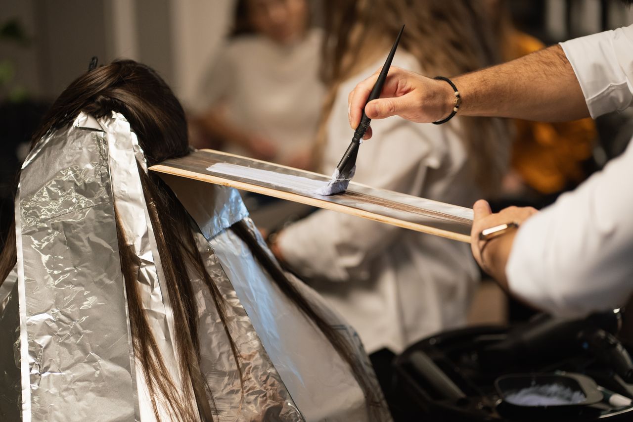 Hairdresser applying dye to client's hair with precision, showcasing modern salon hair coloring techniques.