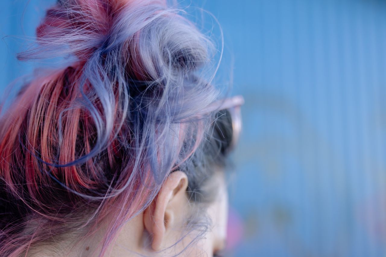 Close-up view of vibrant pink and purple dyed hair against a blue background.